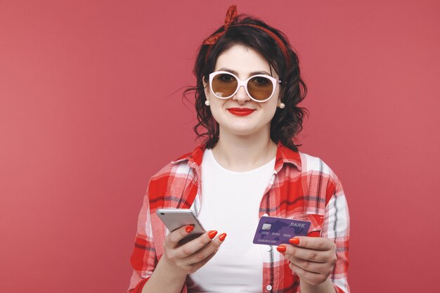 Une femme heureuse détient une carte de crédit. fond rose isolé.