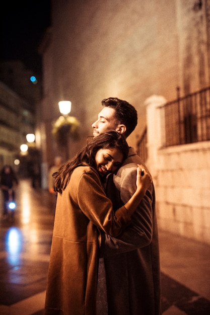Femme heureuse élégante embrassant avec jeune homme sur la promenade de nuit