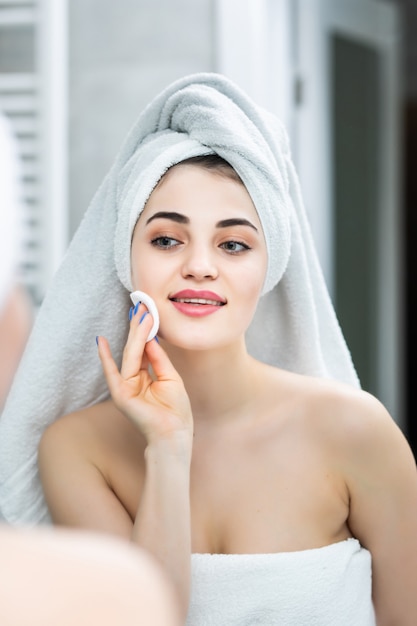 Femme heureuse enlevant le maquillage des tampons nettoyants lotion miroir de salle de bain dans la salle de bain