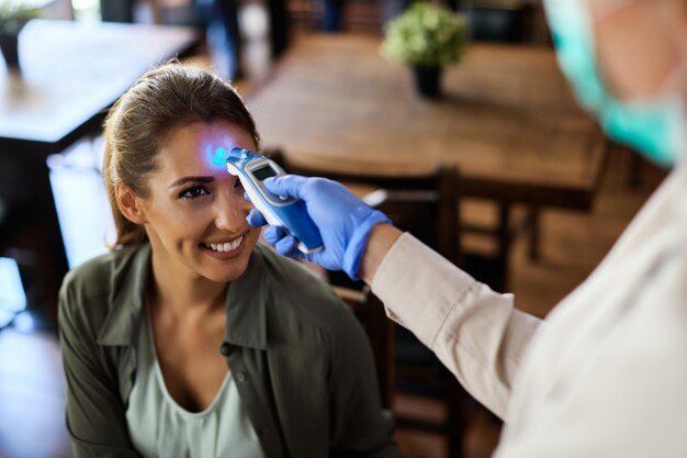 Femme heureuse faisant mesurer sa température avec un thermomètre infrarouge dans un café