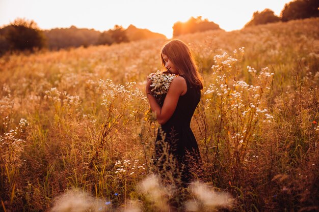 Femme heureuse avec des fleurs se dresse sur le champ de la soirée