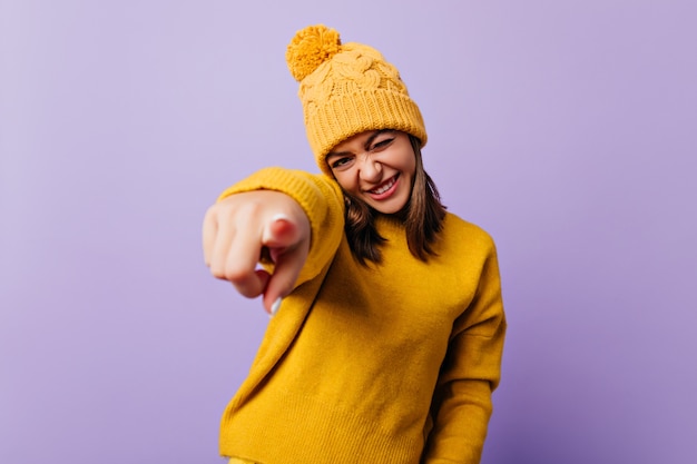 Une femme heureuse et pleine d'esprit clignote et sourit amicalement. Portrait de blogueur élégant pointant vers l'avant