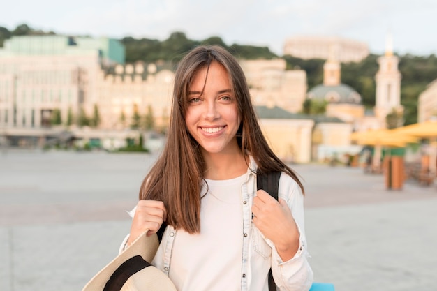 Femme heureuse posant à l'extérieur avec chapeau et sac à dos