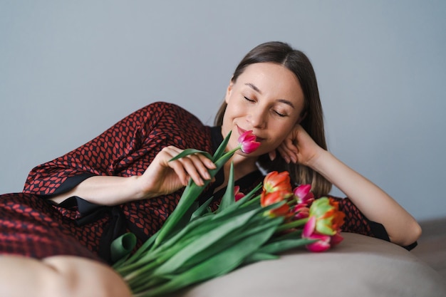 Femme heureuse profitez d'un bouquet de tulipes Femme au foyer bénéficiant d'un bouquet de fleurs tout en vous relaxant sur un pouf confortable