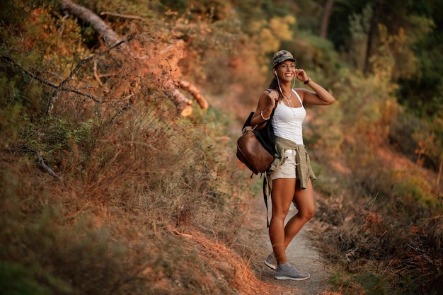 Femme heureuse en randonnée tout en écoutant de la musique sur des écouteurs dans la forêt