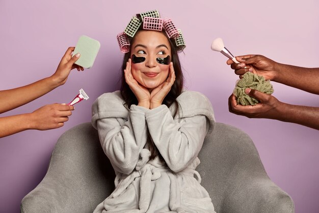 Femme heureuse rêveuse pose avec des patchs pour les yeux et des bigoudis