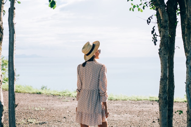 Femme heureuse en robe mignonne d'été et chapeau de paille en vacances avec vue exotique tropicale