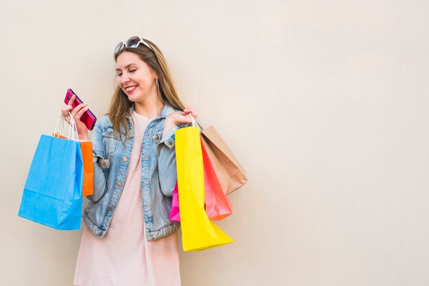 Femme heureuse avec des sacs à provisions à l&#39;aide de smartphone