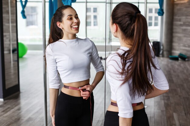 Femme heureuse se regarde dans le miroir tenant un ruban à mesurer à la taille