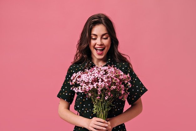 Une femme heureuse en tenue à pois tient un bouquet sur un mur rose