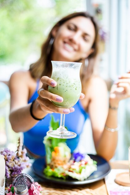 Femme heureuse tient du thé vert matcha japonais avec de la glace en verre au café Femme avec une boisson antioxydante saine en été café mignon