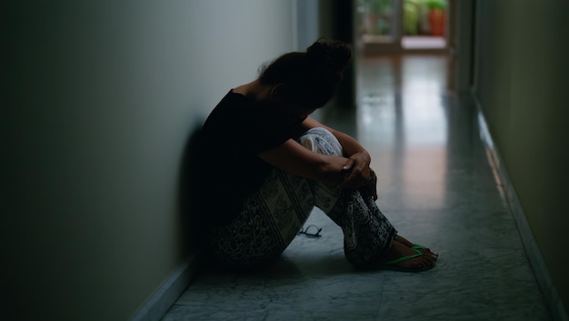 Une femme hispanique d'âge moyen souffrant de violence domestique avec des ecchymoses sur les yeux assise sur le sol à la maison.