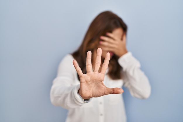 Femme hispanique debout sur fond isolé couvrant les yeux avec les mains et faisant un geste d'arrêt avec une expression de tristesse et de peur. concept embarrassé et négatif.