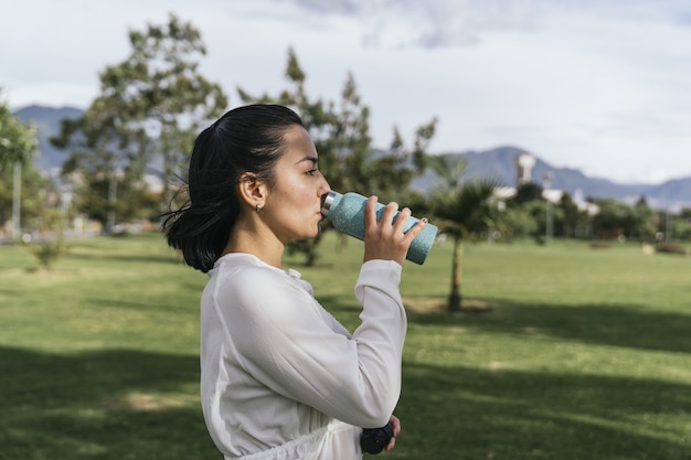 Femme hispanique se reposant en buvant de l'eau après la pratique du yoga