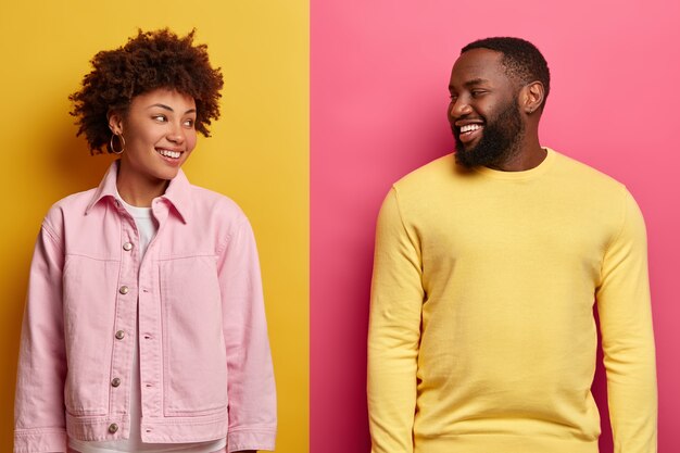 Une femme et un homme afro-américains joyeux se regardent, ont de grands sourires à pleines dents, passent du temps libre, heureux après le shopping