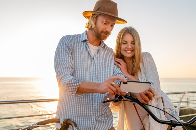 Femme et homme amoureux voyageant à vélo au coucher du soleil sur la mer