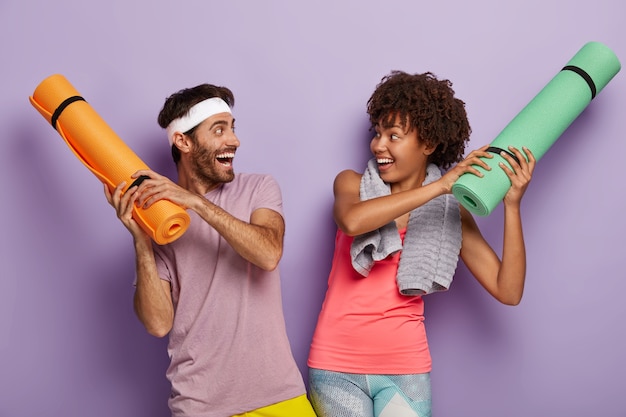 Une femme et un homme heureux ont une humeur ludique, ont des expressions heureuses, ont enroulé des karemats, habillés de vêtements décontractés