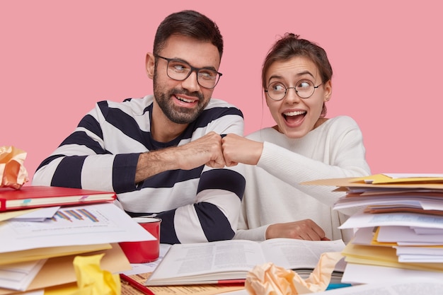 Une femme et un homme heureux se donnent le poing l'un à l'autre, travaillent en équipe amicale, acceptent de collaborer, entourés de manuels et de documents contenant des données et des graphiques