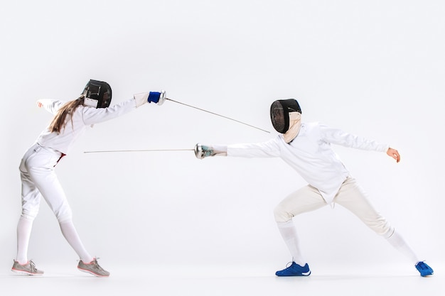 La femme et l'homme portant un costume d'escrime pratiquant avec l'épée contre le gris