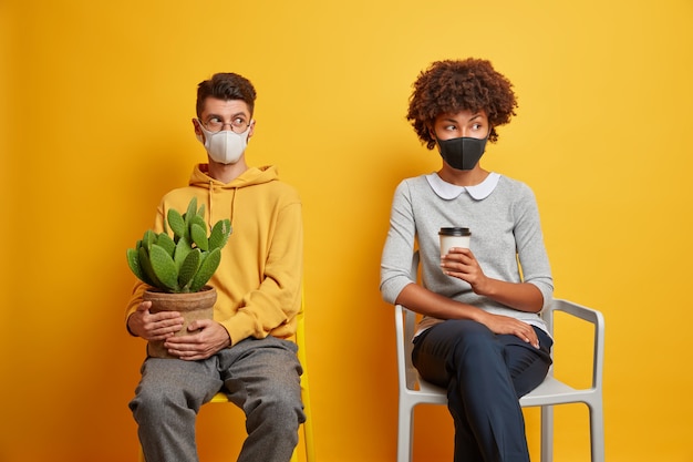 Photo gratuite la femme et l'homme qui s'ennuient restent à la maison pendant la quarantaine, porter des masques pour boire du café et porter des cactus en pot s'asseoir sur des chaises confortables