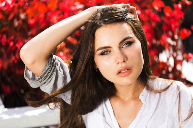 La femme impressionnante aux yeux verts est assise devant les fleurs rouges