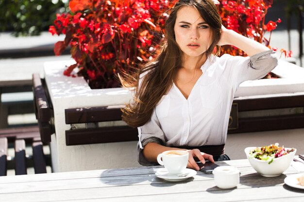 La femme impressionnante aux yeux verts est assise devant les fleurs rouges