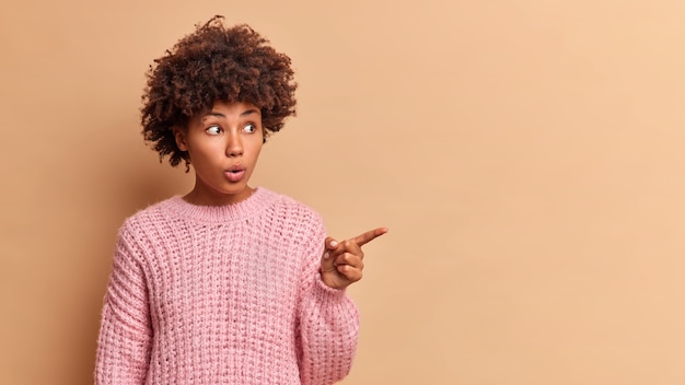 Photo gratuite une femme impressionnée stupéfaite par des points d'offre incroyables sur un espace vide retient le souffle ouvre la bouche d'étonnement porte un pull tricoté isolé sur un mur beige