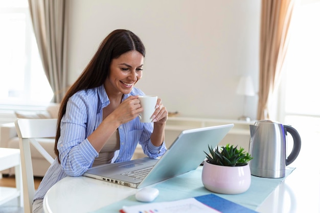 Femme indépendante travaillant avec son ordinateur portable à la maison avec une tasse de café