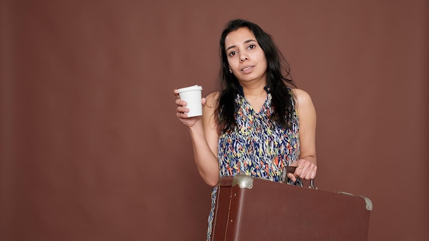 Femme indienne se prépare à voyager en vacances avec valise et tasse de café à la main. Se sentir heureux de partir en vacances avec une valise et une boisson.