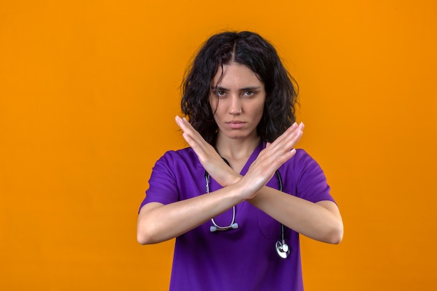 Photo gratuite femme infirmière en uniforme médical et avec stéthoscope croisant les mains faisant signe négatif de refus debout avec une expression de colère sur jaune isolé