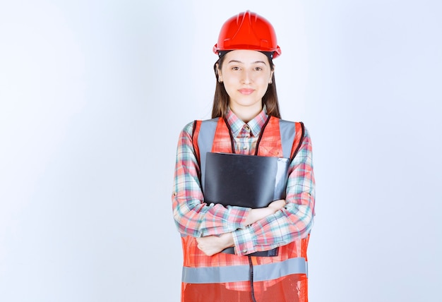 Femme ingénieur en casque rouge tenant un plan de projet noir.
