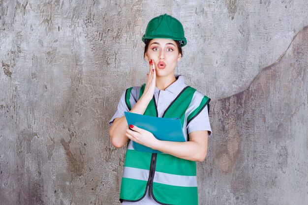 Femme ingénieur en casque vert tenant un dossier bleu