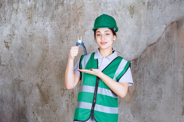 Femme ingénieur en casque vert tenant des pinces pour un travail de réparation.