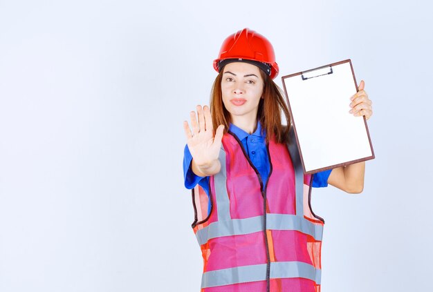 Femme ingénieur en uniforme tenant un fichier de rapport vierge et arrêtant quelqu'un.