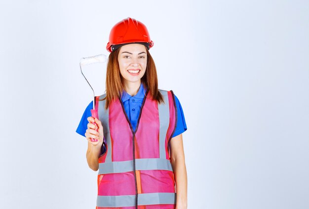 Femme ingénieur en uniforme tenant un rouleau de peinture de couleur blanche.