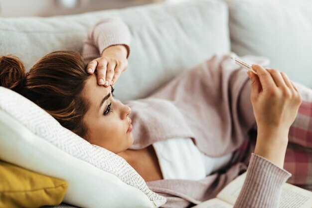 Femme inquiète ayant une forte fièvre tout en mesurant sa température à la maison