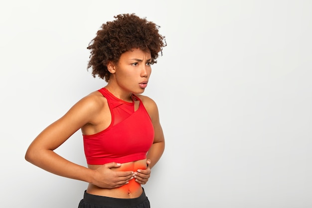 Une femme insatisfaite souffre de sensations douloureuses dans l'estomac, touche le ventre, respire profondément, a des problèmes de santé, souffre d'étouffement après la course ou l'exercice physique