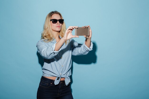 Femme insouciante en chemise et lunettes de soleil faisant selfie sur smartphone