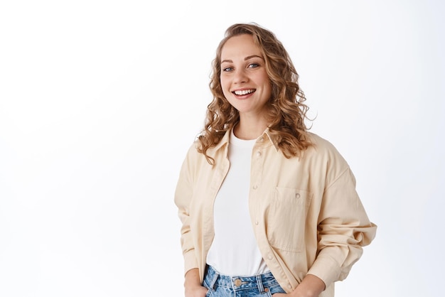 Femme insouciante avec une coiffure bouclée blonde debout détendue et décontractée sur fond blanc souriant heureux espace de copie