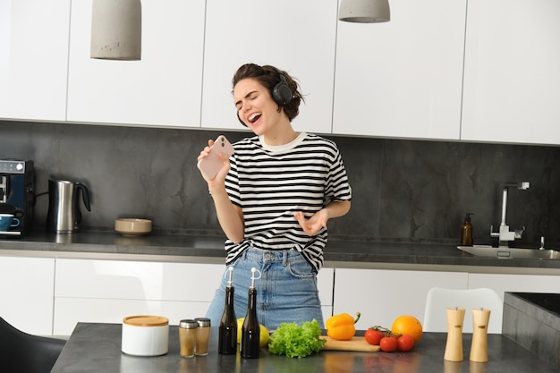 Une femme insouciante cuisinant dans la cuisine chantant sa chanson préférée écoutant de la musique sans fil