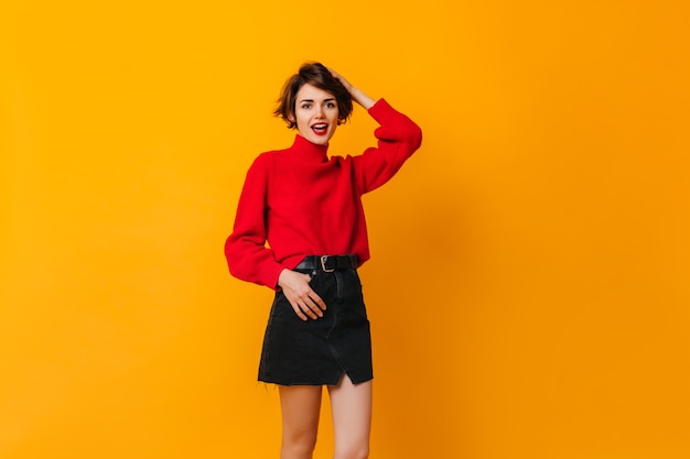 Femme insouciante en jupe debout sur un mur jaune