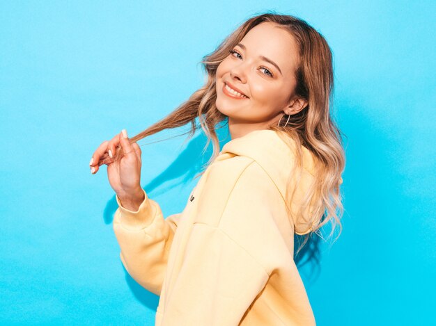 femme insouciante posant près du mur bleu en studio. Modèle positif s'amusant. Touche ses cheveux