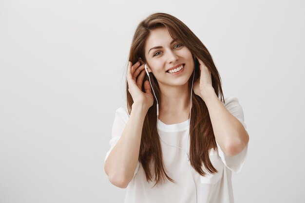 Femme insouciante souriante, écouter de la musique dans des écouteurs