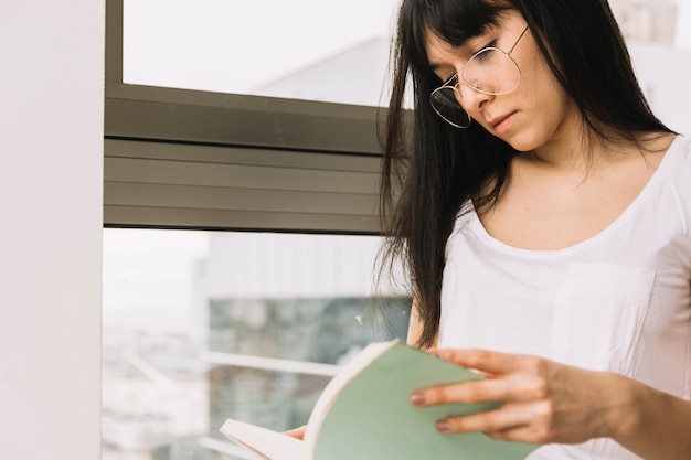 Femme intelligente lisant près de la fenêtre