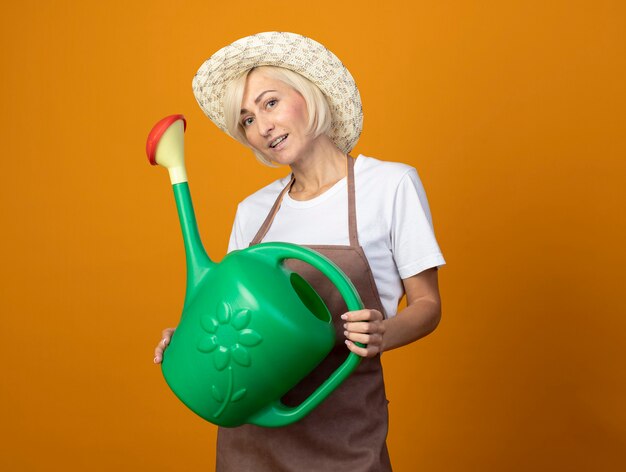 Femme De Jardinier D'âge Moyen Impressionné En Uniforme De Jardinier Portant Un Chapeau Tenant Un Arrosoir