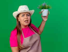 Photo gratuite femme de jardinier d'âge moyen en tablier et chapeau tenant une plante en pot