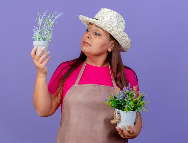 Femme de jardinier d'âge moyen en tablier et chapeau tenant des plantes en pot