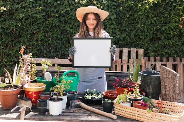 Femme jardinier debout derrière les plantes en pot montrant un cadre blanc