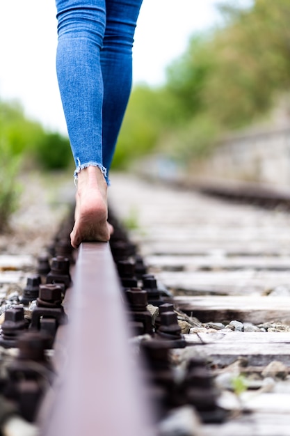 Photo gratuite femme en jeans marchant à travers les rails du train pieds nus