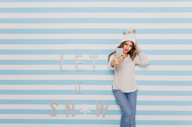 Femme en jeans prenant selfie à côté de l'inscription d'hiver: laissez la neige